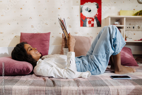 African smiling teen girl liying on bed reading or studying photo