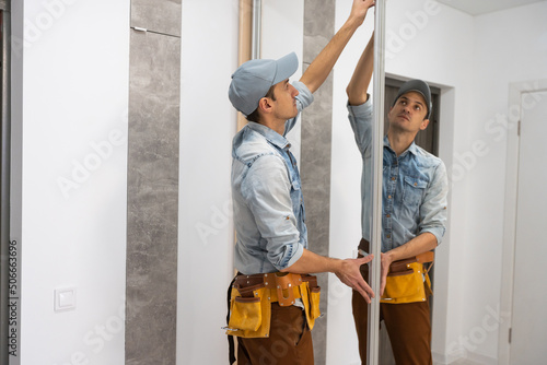 Foto Employee furniture assembler in white t-shirt and jumpsuit checks wooden sliding door of modern wardrobe with mirror