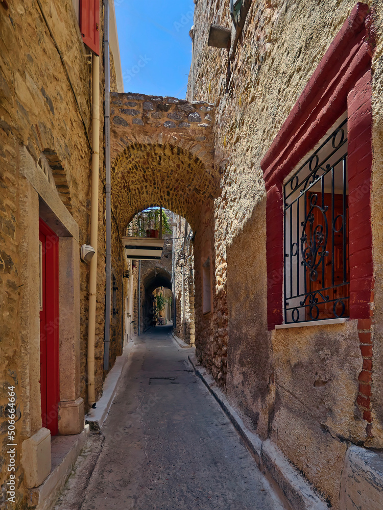 A cobblestone alley between picturesque old stone houses with reddish doors and windows. Pirgi, Chios island, Greece