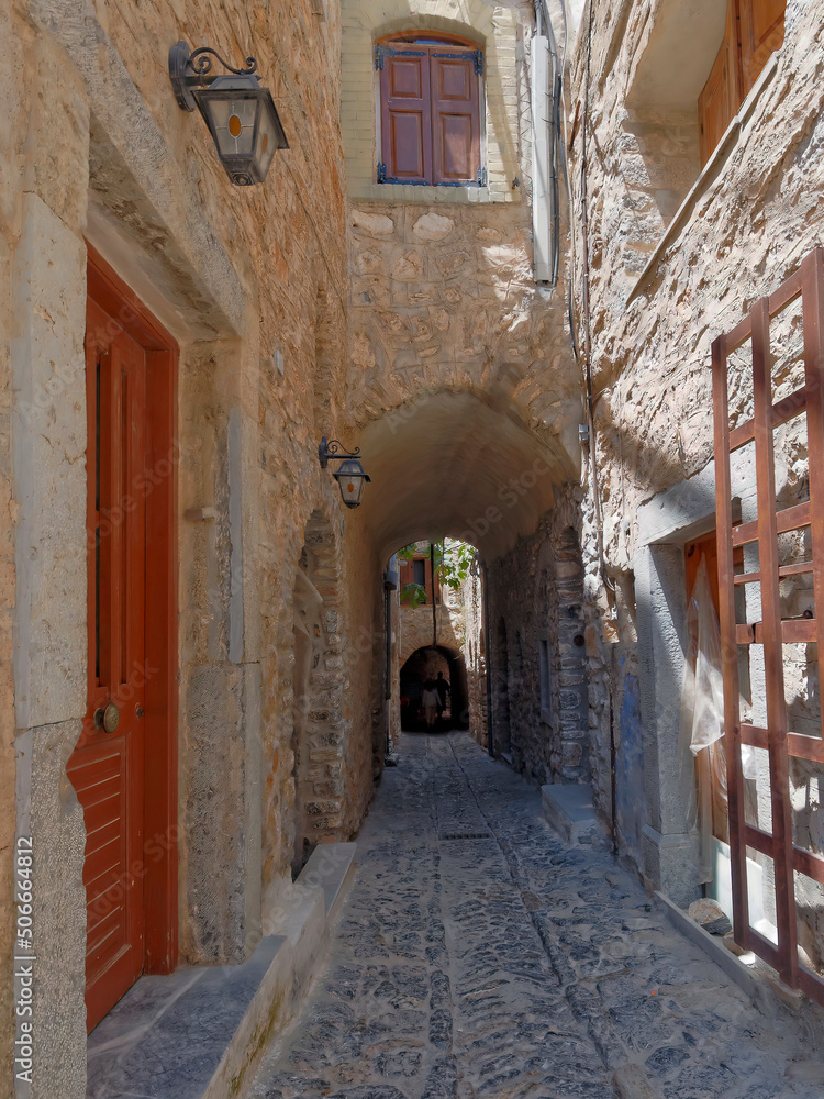 A cobblestone alley between picturesque old stone houses with reddish doors and windiws. Pirgi, Chios island, Greece