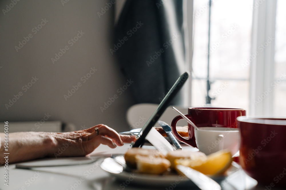 White mature woman using tablet computer while having breakfast