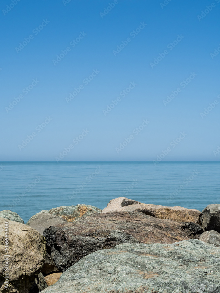 Beautiful marine background. Large boulders in the foreground. Sea, horizon line, blue sky. Summer day. No people. Place for text. Copy space. vertically. Background texture. Background for design.