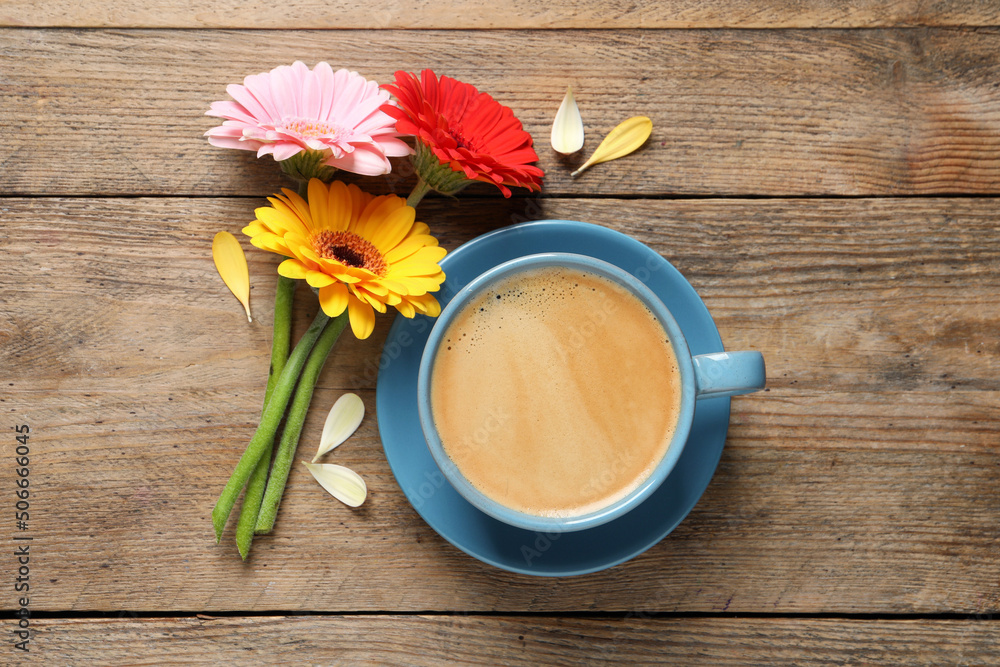 Beautiful colorful gerbera flowers, petals and cup of coffee on wooden table, flat lay
