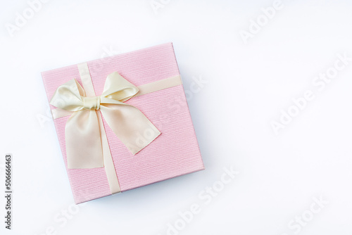 Top view of Delicate pink gift box with satin light ribbon tied in a beautiful bow on a white background. Present for Mother's Day or Women's Day. Copy space, Flat lay style.