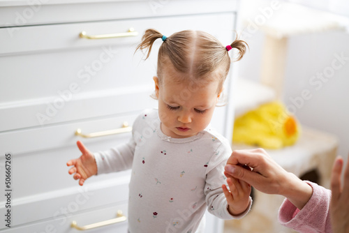 baby girl with two pigtails hold mother hand at natural home background