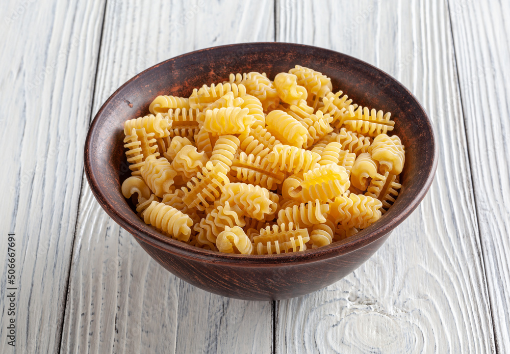 Uncooked radiatori pasta in ceramic bowl on white wooden background Uncooked radiatori pasta in ceramic bowl on white wooden background