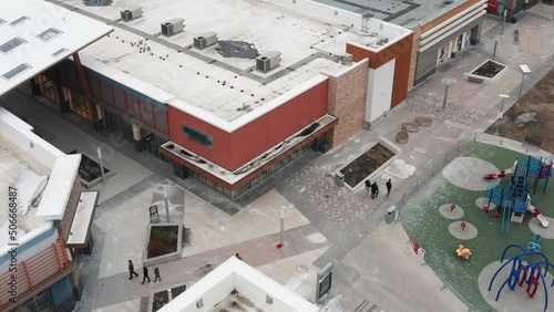 People walking through outdoor mall beside play structure in winter entering stores