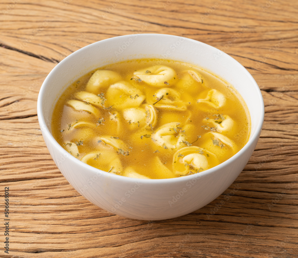 Cappelletti or tortellini brodo soup in a bowl over wooden table Cappelletti or tortellini brodo soup in a bowl over wooden table