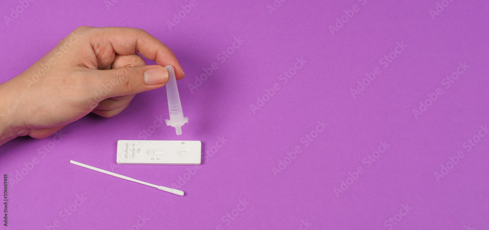 Obraz premium A hand is holding an antigen extraction tube and antigen test device, Sterlized Swab on the floor with a violet background..