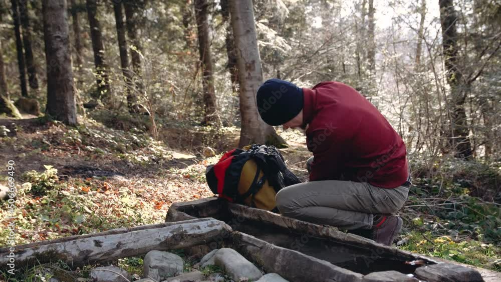 touristin the woods near a stream, spring water, takes a mug from his backpack. touristin the woods near a stream, spring water, takes a mug from his backpack.