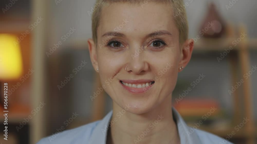 Portrait of caucasian young woman with short haircut looking at camera in comfortable apartment. Charming female with piercing in nose and ears posing on cozy couch. Portrait of caucasian young woman with short haircut looking at camera in comfortable apartment. Charming female with piercing in nose and ears posing on cozy couch.