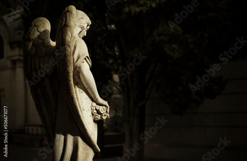 Old statue of angel in cemetery with sunlight and shadow