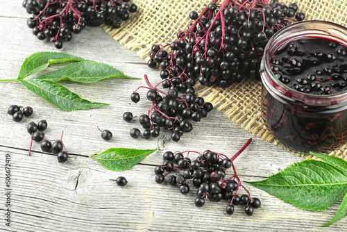 Fresh ripe black elderberries, elderberry syrup and leaves of elderberry on rustic wooden boards background. Alternative medicine and lifestyle.