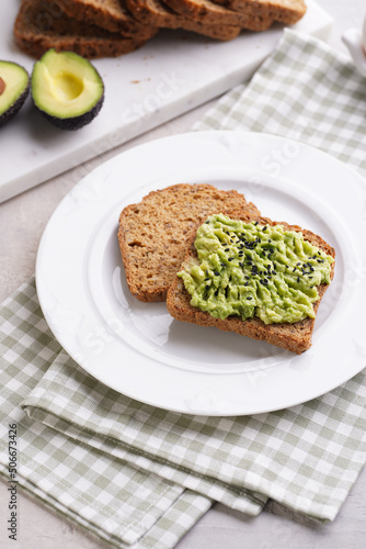 Slices of gluten-free sunflower seeds bread with avocado and sesame seeds on white plate on green checkered napkin
