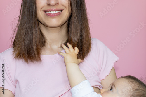 happy smiling young mother breastfeeding her little baby boy or girl. adorable toddler playing with hair.child care. pink background, isolated. child with 2 swirls,whorls,on head. motherhood concept photo