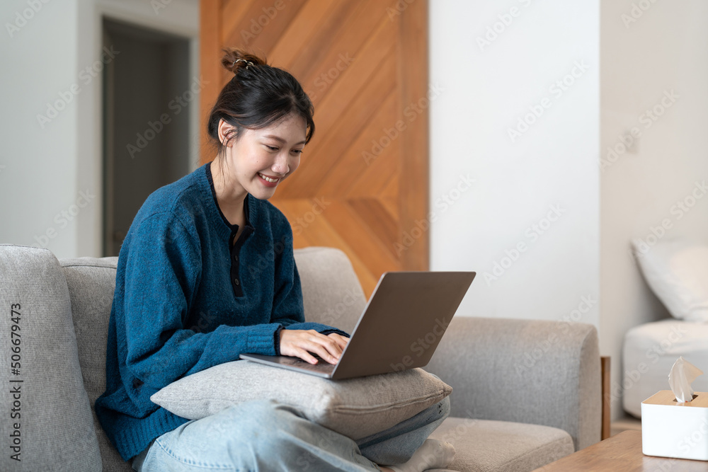 Young asian woman using laptop in the sofa with a happy face standing and smiling with a confident smile showing teeth Young asian woman using laptop in the sofa with a happy face standing and smiling with a confident smile showing teeth
