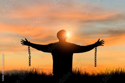 Silhouette of freedom young man standing alone with beautiful sky at sunset open both arms with chains on his arms. He felt free from the shackles tied to his arms.