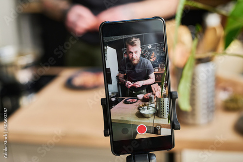 Horizontal selective focus close-up of food blogger filming content on smartphone camera using tripod photo