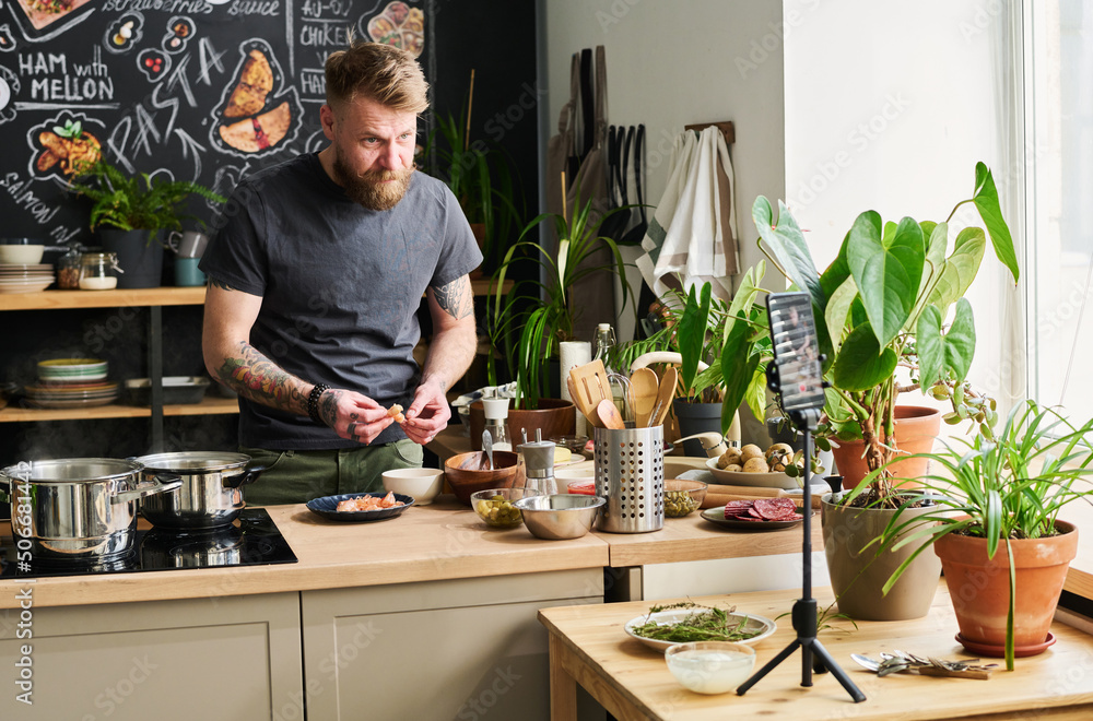 Handsome bearded Caucasian man standing in loft kitchen cooking dinner on camera peeling shrimps Handsome bearded Caucasian man standing in loft kitchen cooking dinner on camera peeling shrimps