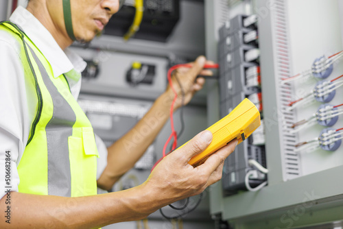 Electrical engineer or repairman holding digital multimeter to inspecting the electrical system in a factory.