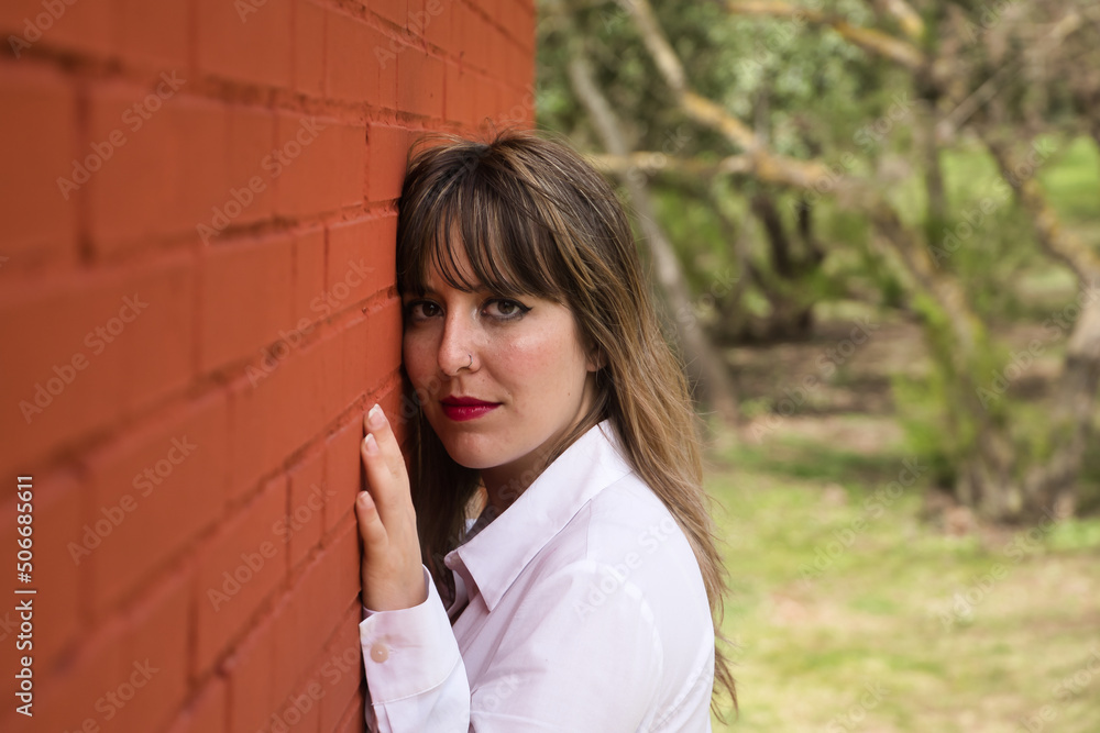 Portrait of young, pretty, blonde woman in white shirt with face leaning against a red brick wall, looking serious . Concept beauty, fashion, portrait, seriousness. Portrait of young, pretty, blonde woman in white shirt with face leaning against a red brick wall, looking serious . Concept beauty, fashion, portrait, seriousness.
