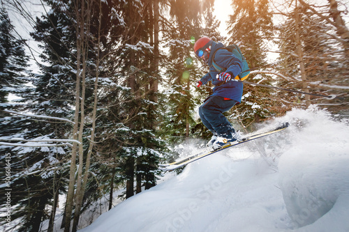 A male athlete skier rides a freeride in a winter forest in the mountains. Jump against the backdrop of snow-covered trees and the setting sun