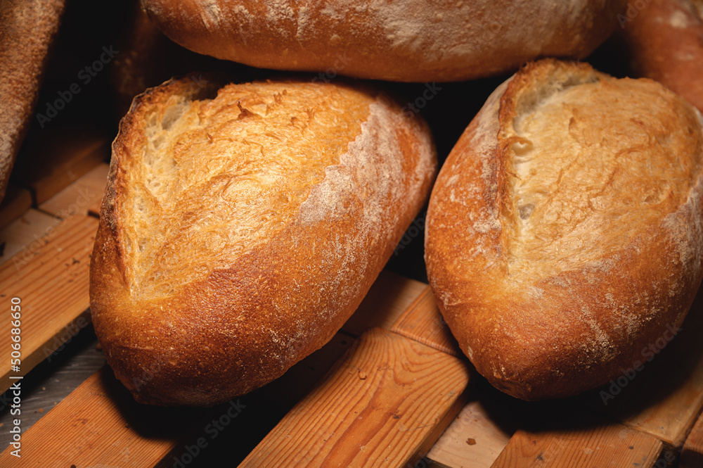 Fresh crispy hot delicious craft artisan bread. Many loaves lie on a wooden pallet Fresh crispy hot delicious craft artisan bread. Many loaves lie on a wooden pallet