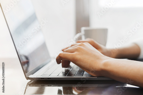 Close up of a young woman's hands typing on a laptop in a coffee shop. Freelancer works in a cafe. Laptop, hands and coffee mug.