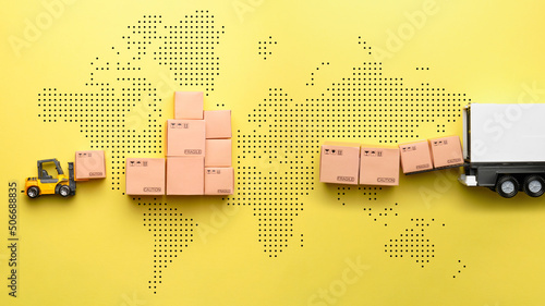 The concept of logistics and delivery of goods. A loader loads goods into a truck against the backdrop of a world map.