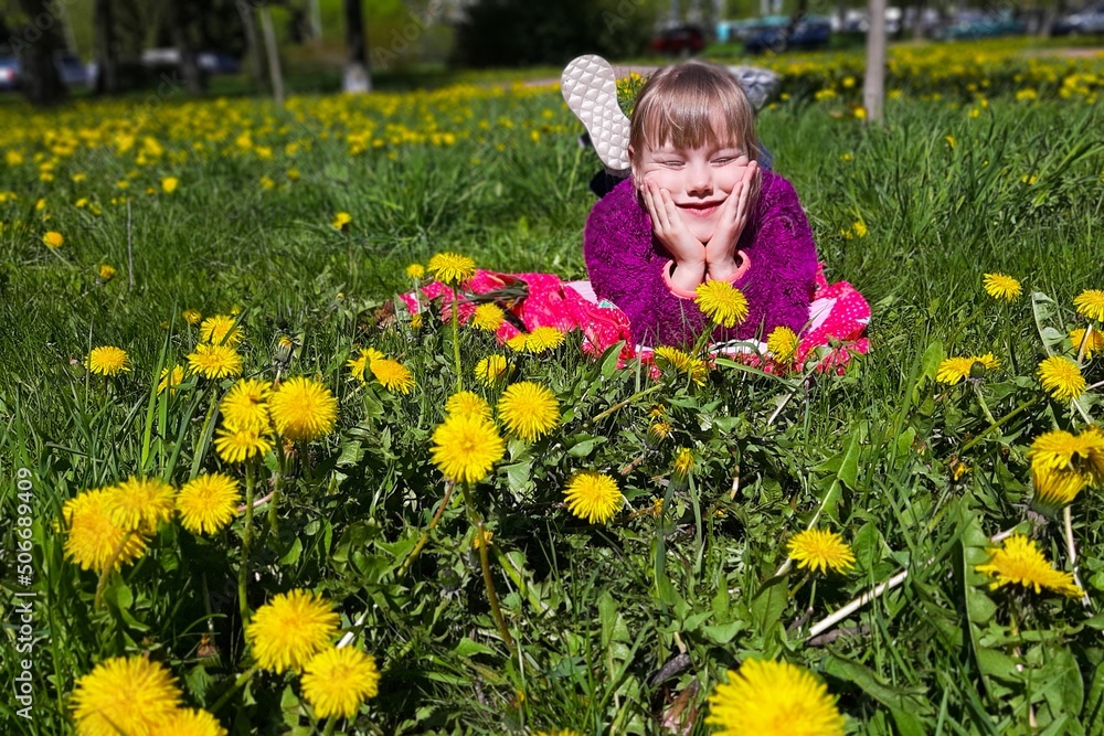 Cute little girl lies on grass in park. There are dandelions all around. Cute little girl lies on grass in park. There are dandelions all around.