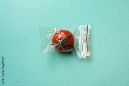 Red tomato in a zip bag on a green background, the concept of excess food packaging