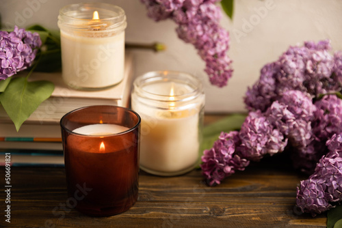 Cozy home decor. Burning aroma candles on the background of wooden textures.Composition with eco candles and a bouquet of spring lilac.Aromatherapy and relaxation.