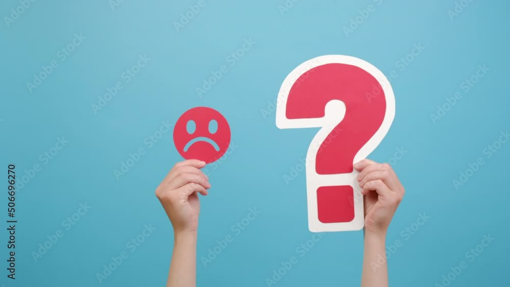 Female hand holding red unsatisfied face emoticon and question mark sign, isolated on blue color background wall in studio with copy space for promotion content. Concept stressed business and thoughts Female hand holding red unsatisfied face emoticon and question mark sign, isolated on blue color background wall in studio with copy space for promotion content. Concept stressed business and thoughts