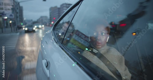 Medium shot of young black woman sitting inside a taxi uber going through the city on early morning