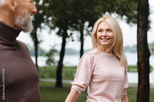 Love and relationship. Caucasian mature couple walking together on a date, looking at each other, holding hands in city park outdoors.