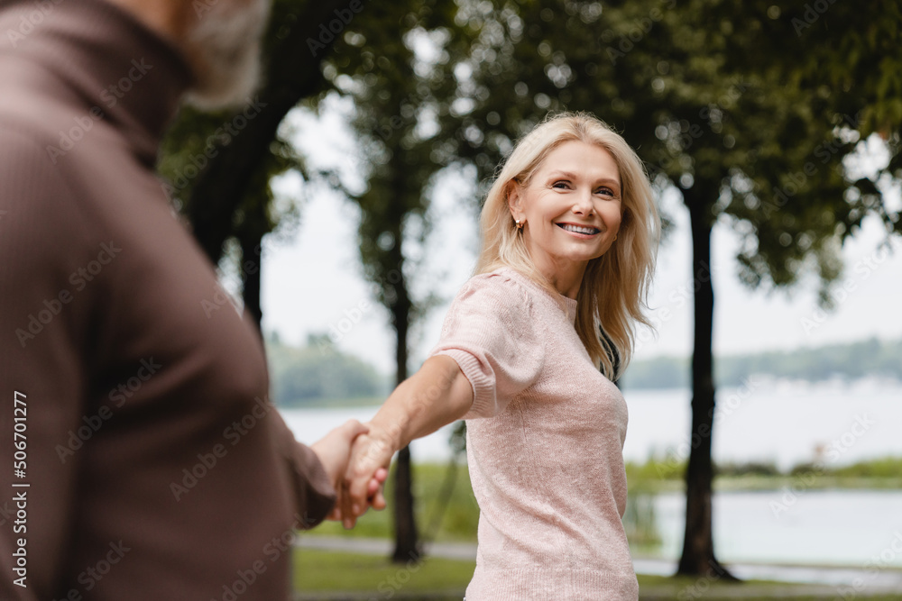 Obraz premium Caucasian mature heterosexual couple spouses wife and husband walking on a romantic date, holding hands, enjoying moments together in park.