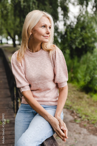 Vertical portrait of a caucasian mature beautiful blonde woman wife walking alone in park forest outdoors spending free time in woods. #506701892