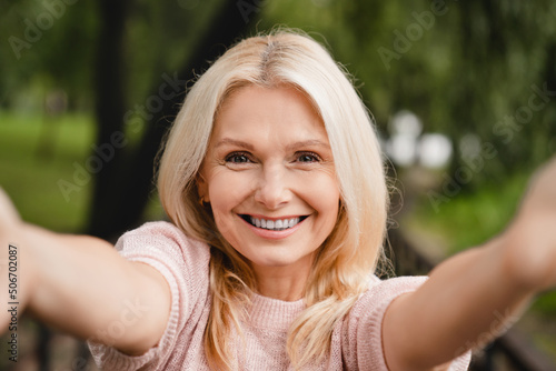Cheerful caucasian mature woman taking selfie photo on smartphone, vlogging, blogging, having video call while walking in park forest