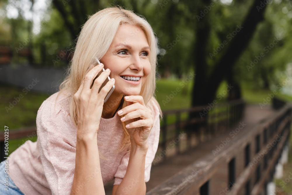 Closeup cropped shot of mature caucasian woman talking on smart phone, calling her friends husband colleagues with good connection in park outdoors.