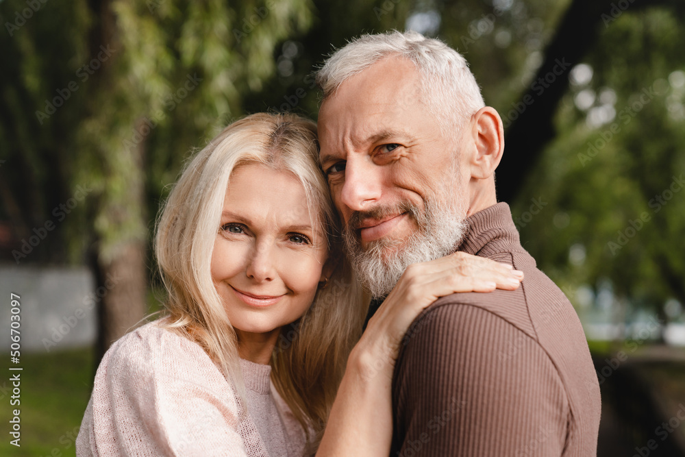 Confident happy cheerful mature couple embracing hugging each other looking at the camera with love and passion. Protection and trust concept. Confident happy cheerful mature couple embracing hugging each other looking at the camera with love and passion. Protection and trust concept.
