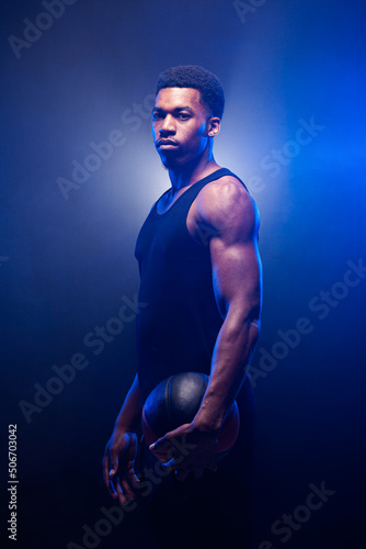 Obraz na plátně Basketball player lit with blue color holding a ball against smoke background