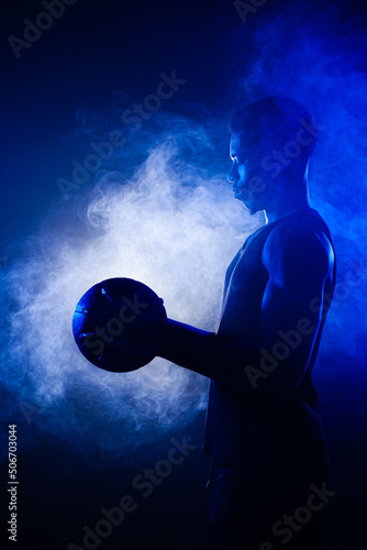 Basketball player holding a ball against blue fog background. African american man silhouette.