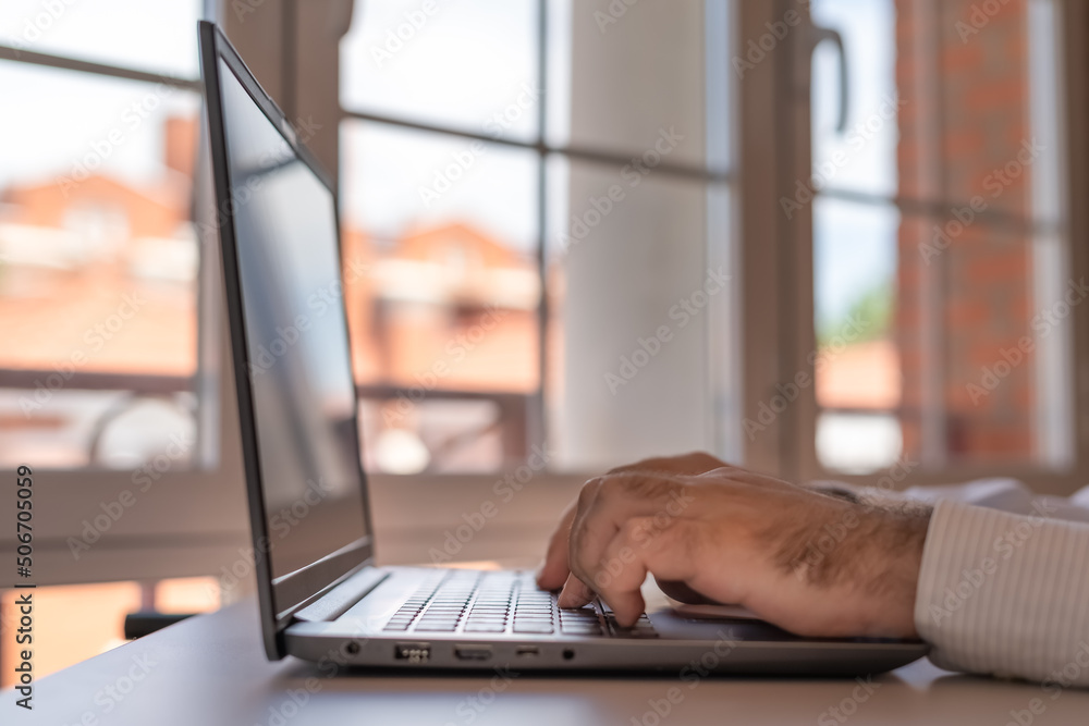 Man working on a laptop in his house with large windows of light. Man working on a laptop in his house with large windows of light.