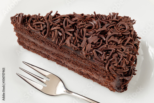 Slice of chocolate cake with cream filling and chocolate shavings next to fork from above. photo