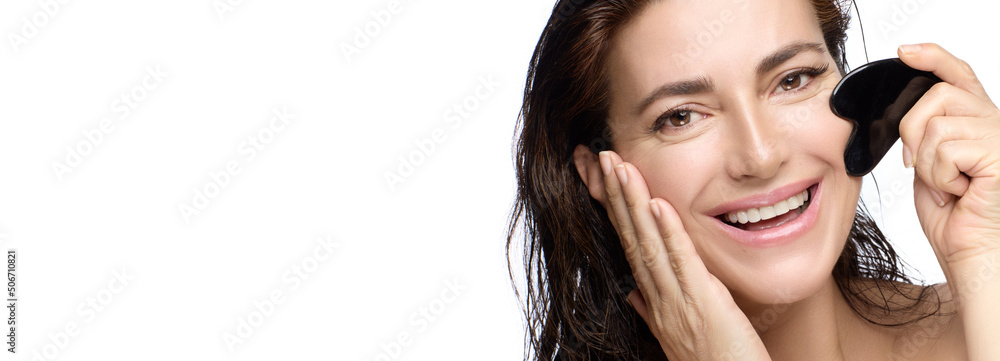 Beauty and skin care concept. Happy woman with healthy glowing skin using a Gua sha stone Beauty and skin care concept. Happy woman with healthy glowing skin using a Gua sha stone