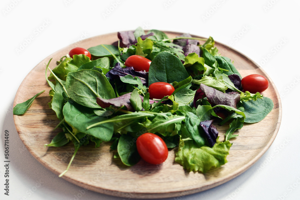 Fresh green salad with spinach, arugula, romaine and lettuce, decorated with cherry tomatoes, on wooden plate Fresh green salad with spinach, arugula, romaine and lettuce, decorated with cherry tomatoes, on wooden plate