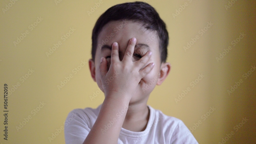 Cute boy smiling and covering his face on colour background Cute boy smiling and covering his face on colour background