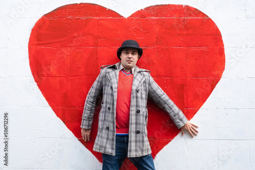 The concept of unhappy love. Frightened man stands against the background of a red heart painted on a white wall