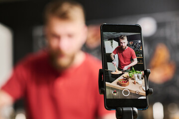 Selective focus shot of modern Caucasian food blogger cooking pasta filming process on smartphone camera