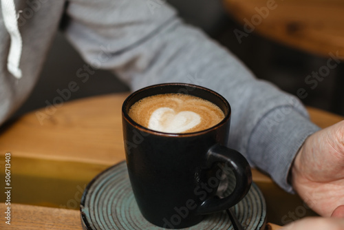 Delicious cappuccino with vegetable milk in a black ceramic cup. A man drinks coffee in a cafe. Beautiful cappuccino serving with almond milk